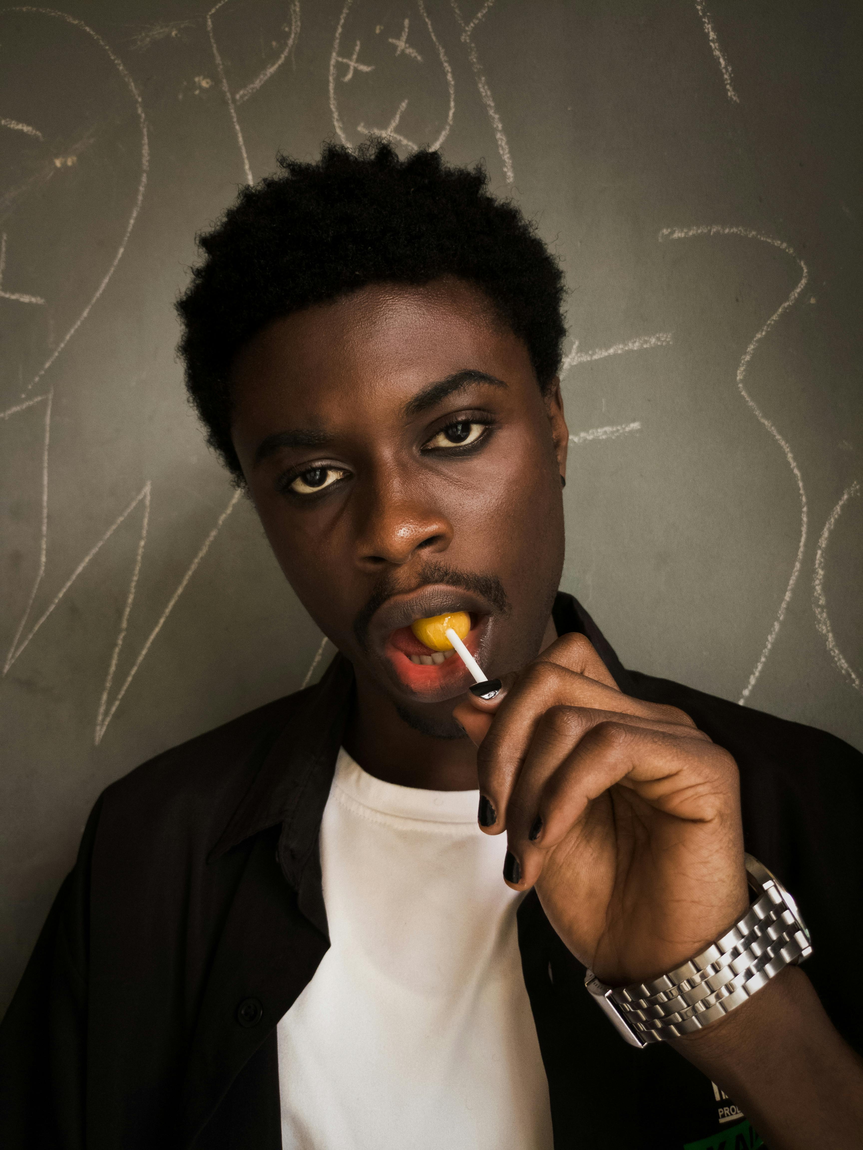 ฟรี ภาพระยะใกล้ของชายหนุ่มกำลังเพลิดเพลินกับการกินอมยิ้ม โดยมีฉากหลังเป็นกระดานดำ คลังภาพถ่าย