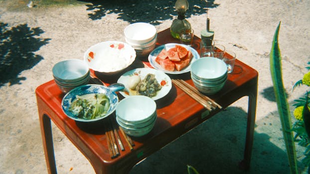 A vibrant spread of Asian dishes on a rustic outdoor table under the sun.