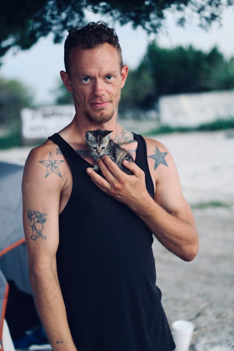 Man Wearing Black Tank Top Carrying Brown Tabby Cat