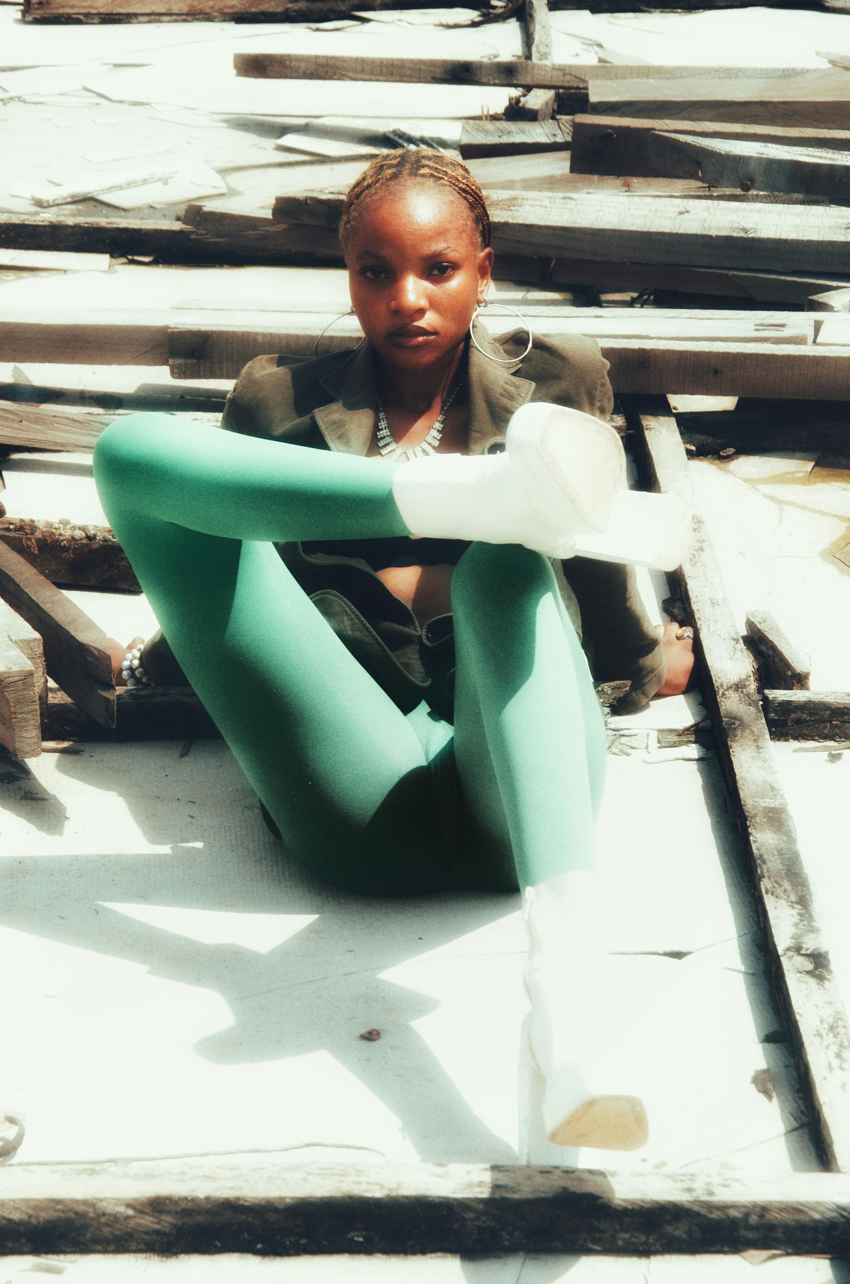 grátis Mulher africana elegante, vestindo leggings verde-vibrantes, posando ao ar livre em um dia ensolarado. Foto profissional