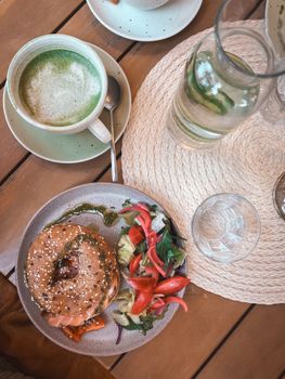 Top view of a healthy breakfast with a bagel, salad, and matcha tea on a wooden table.