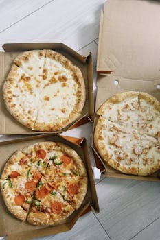Top view of assorted pizzas in cardboard boxes on a wooden floor, ready to eat.