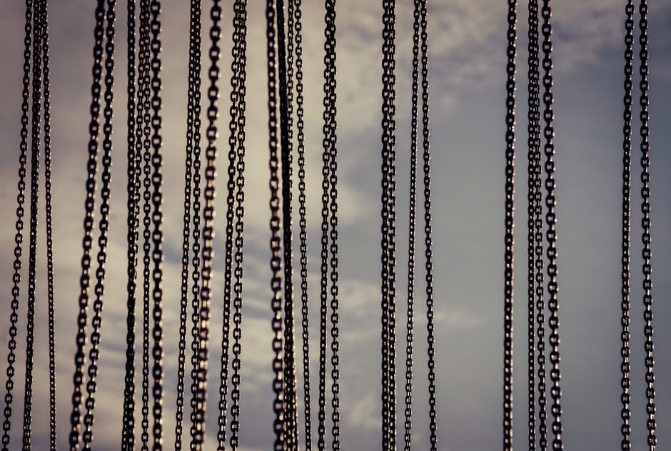 Close-up of metal chains hanging vertically with a cloudy sky in the background.