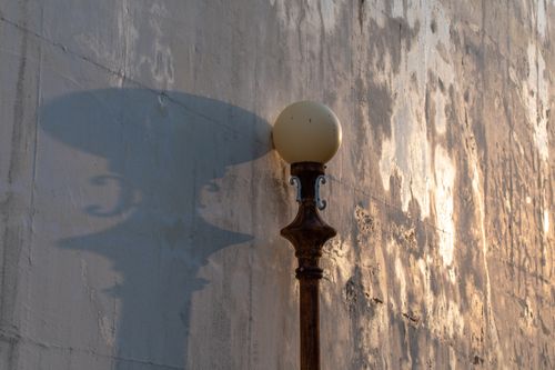 Free Rustic street lamp and its shadow cast on a textured wall in warm light. Stock Photo