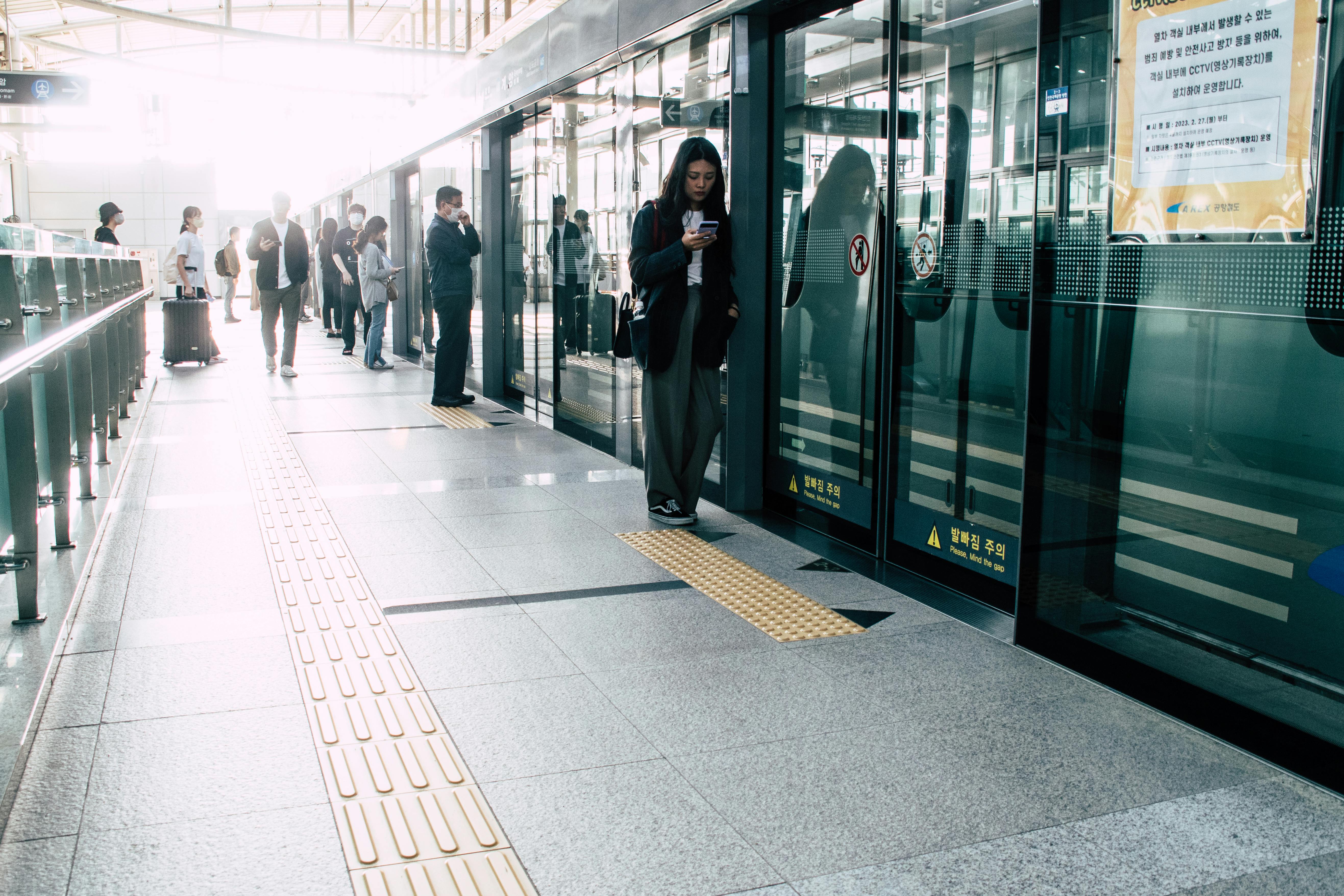 ฟรี ผู้คนเข้าแถวรอรถไฟที่สถานีรถไฟใต้ดินซึ่งสว่างไสว ต่างใช้สมาร์ทโฟนขณะรอรถไฟ คลังภาพถ่าย