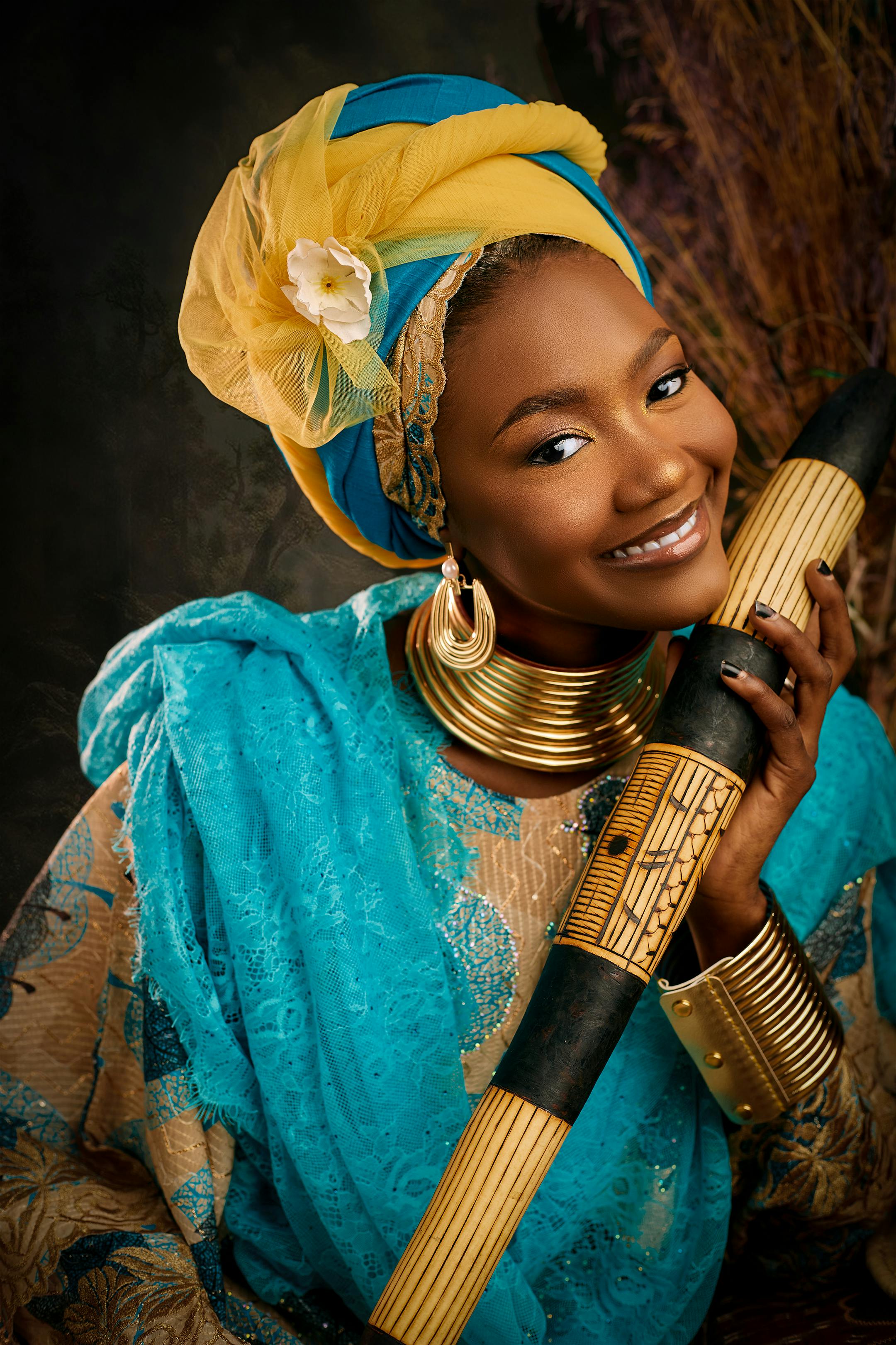 ฟรี หญิงชาวแอฟริกันในชุดสีสันสดใส ถือเครื่องดนตรีพื้นเมือง และยิ้มอย่างอบอุ่น คลังภาพถ่าย