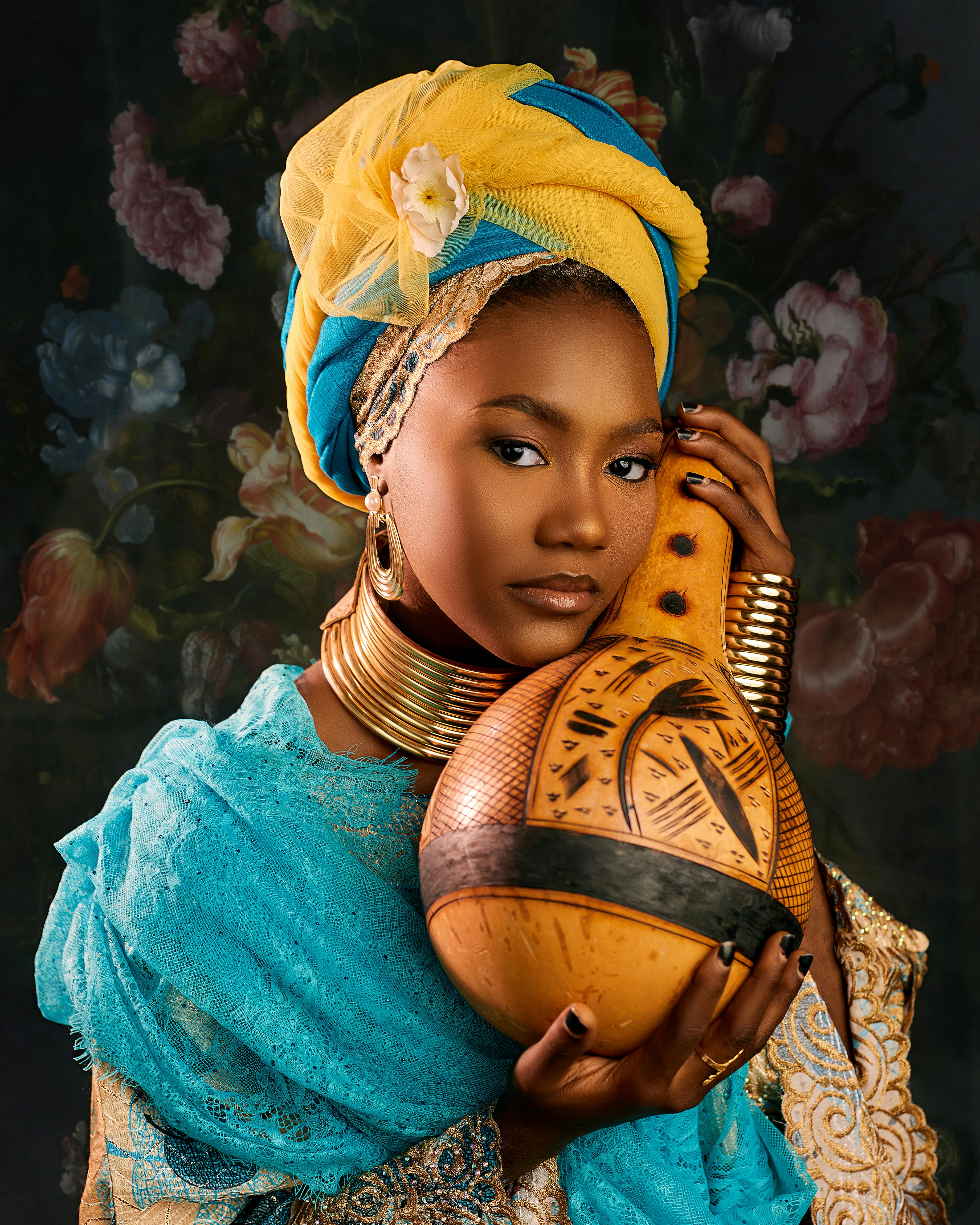 ฟรี ภาพถ่ายหญิงชาวไนจีเรียในชุดพื้นเมืองสีสันสดใส ถือผลน้ำเต้าประดับตกแต่ง โดยมีฉากหลังเป็นลายดอกไม้ คลังภาพถ่าย