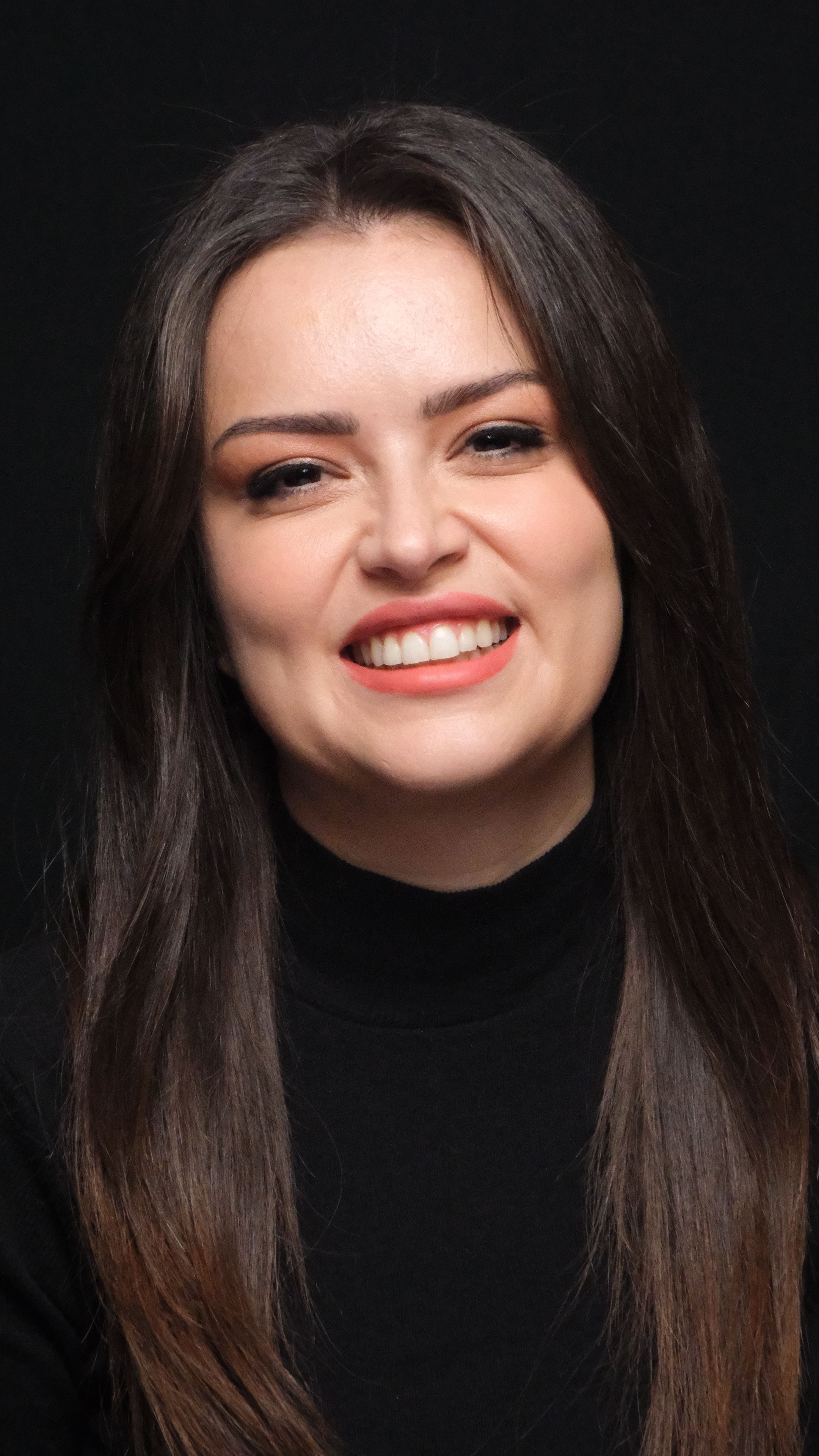 Portrait of a smiling woman with long hair wearing black, captured in studio setting.