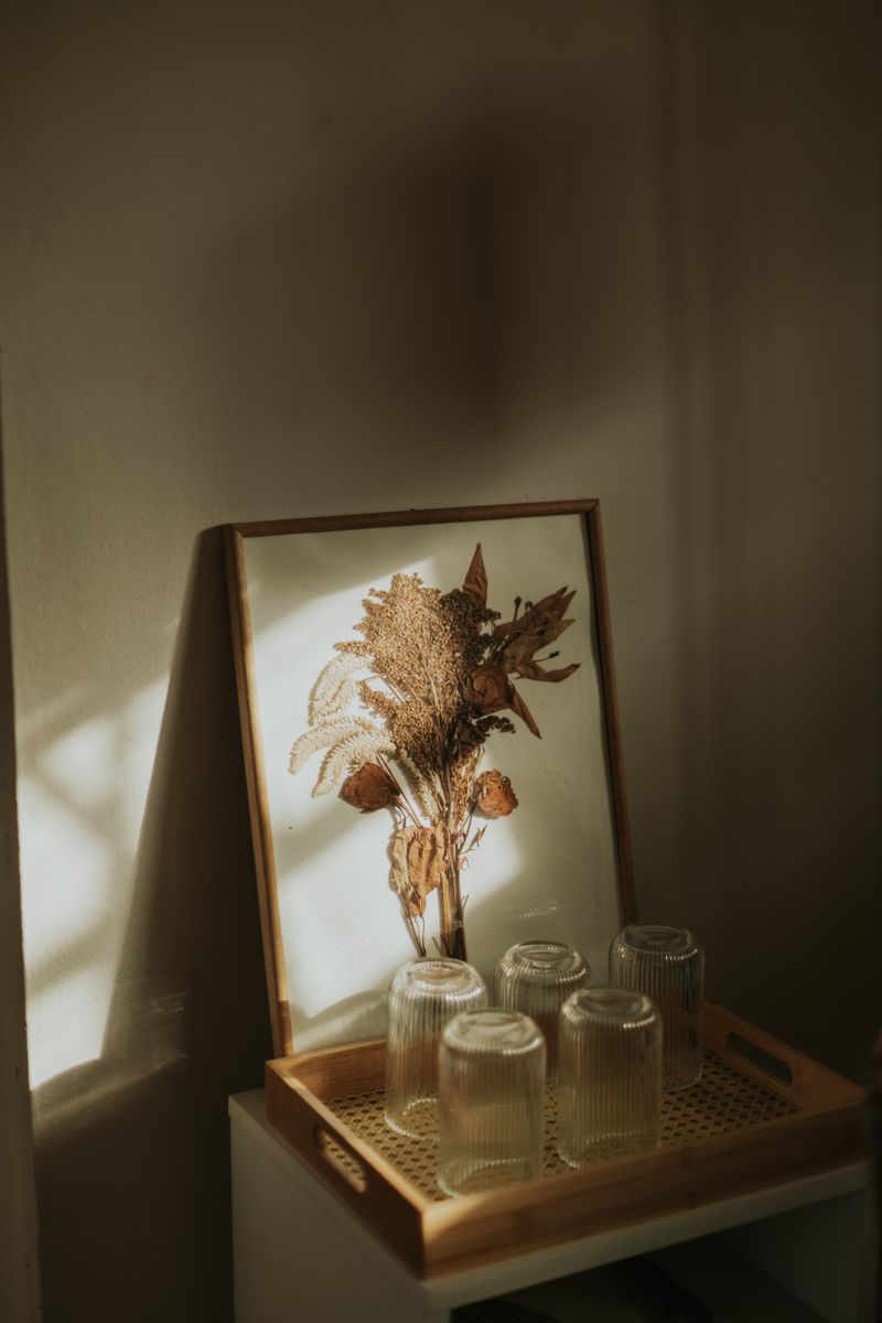 Framed dried flower arrangement with glassware in soft natural light, creating a rustic and elegant decor.