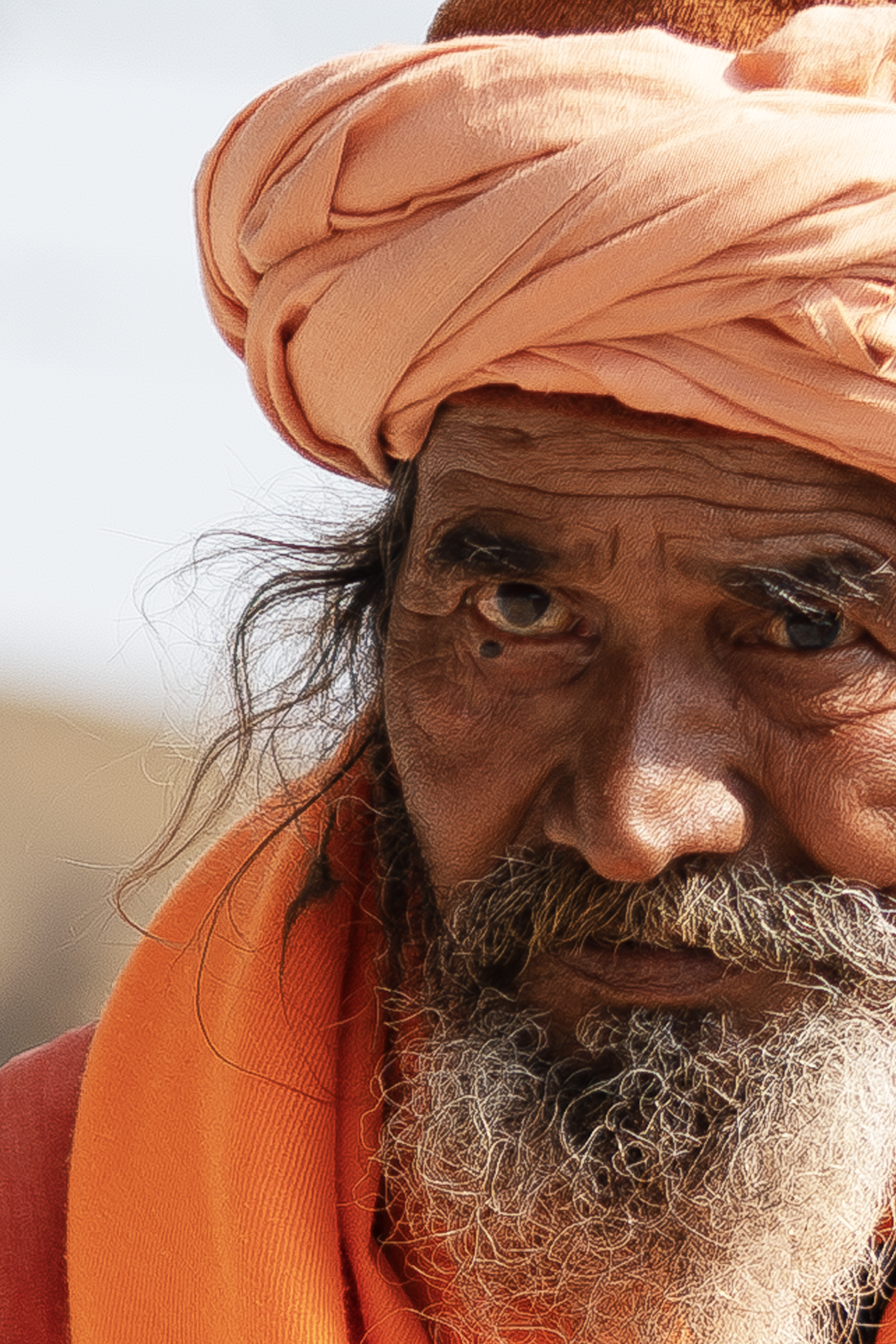 Close-up of an elderly man wearing an orange turban and robe, capturing a deep, thoughtful expression.