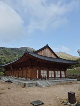 A serene traditional wooden temple set against a lush green mountainous backdrop.