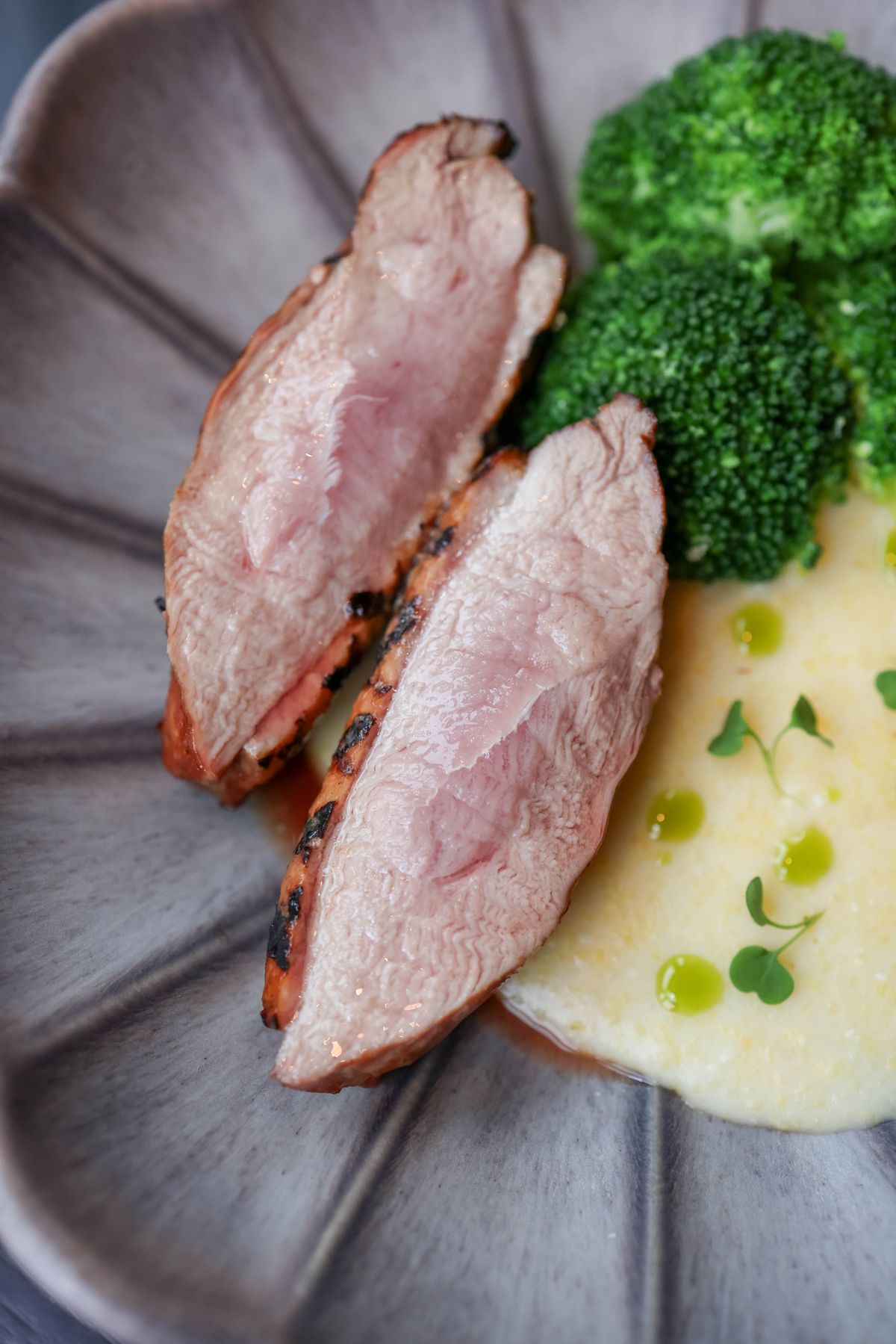 Fine-dining portion of sliced pink duck breast with broccoli and creamy purée on a modern plate — a restaurant-style plating of the classic recipe.