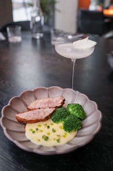 Gourmet plate with pork and broccoli paired with a cocktail in an elegant restaurant setting.