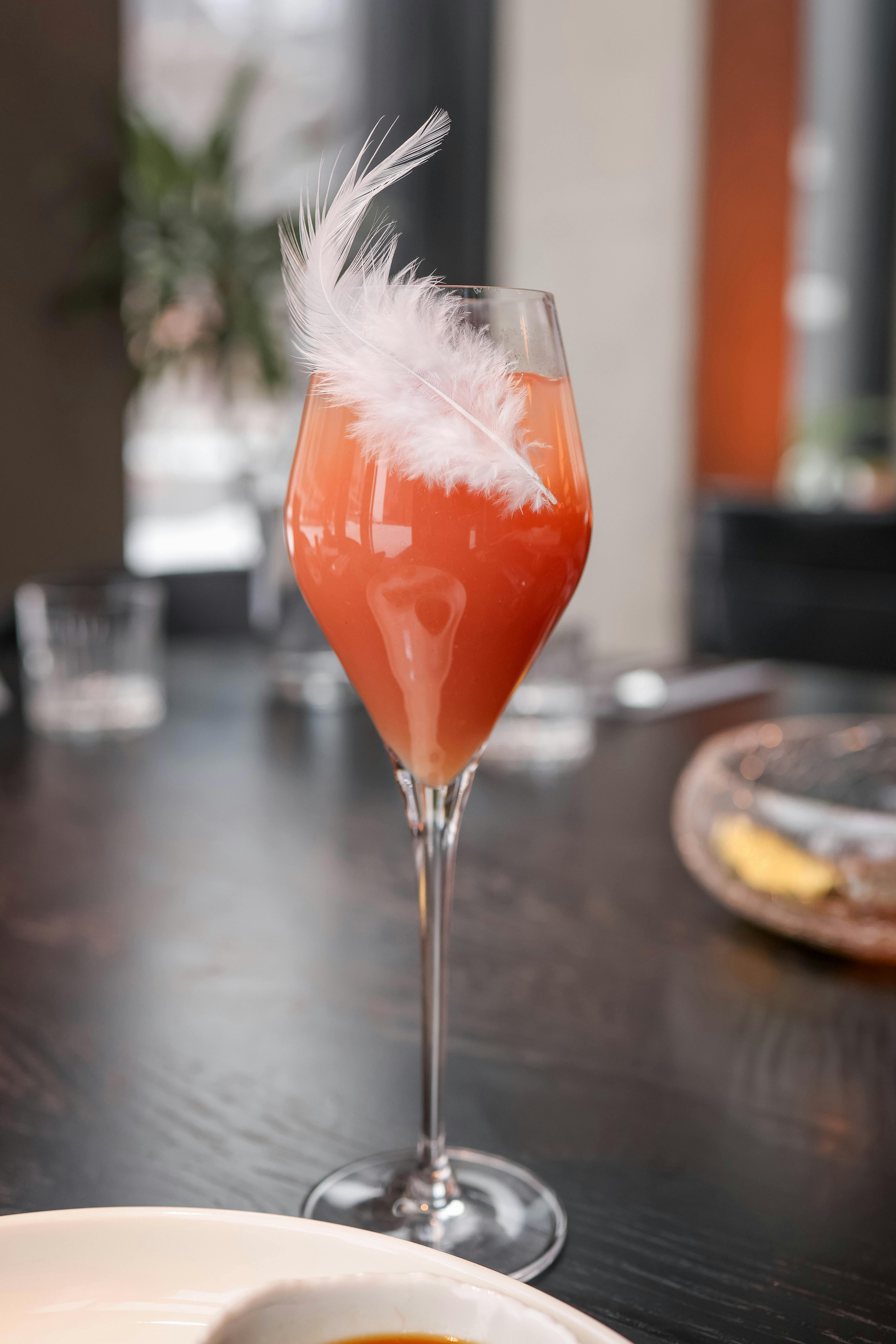 A stylish cocktail served in a wine glass with a feather garnish. Ideal for lifestyle and culinary themes.