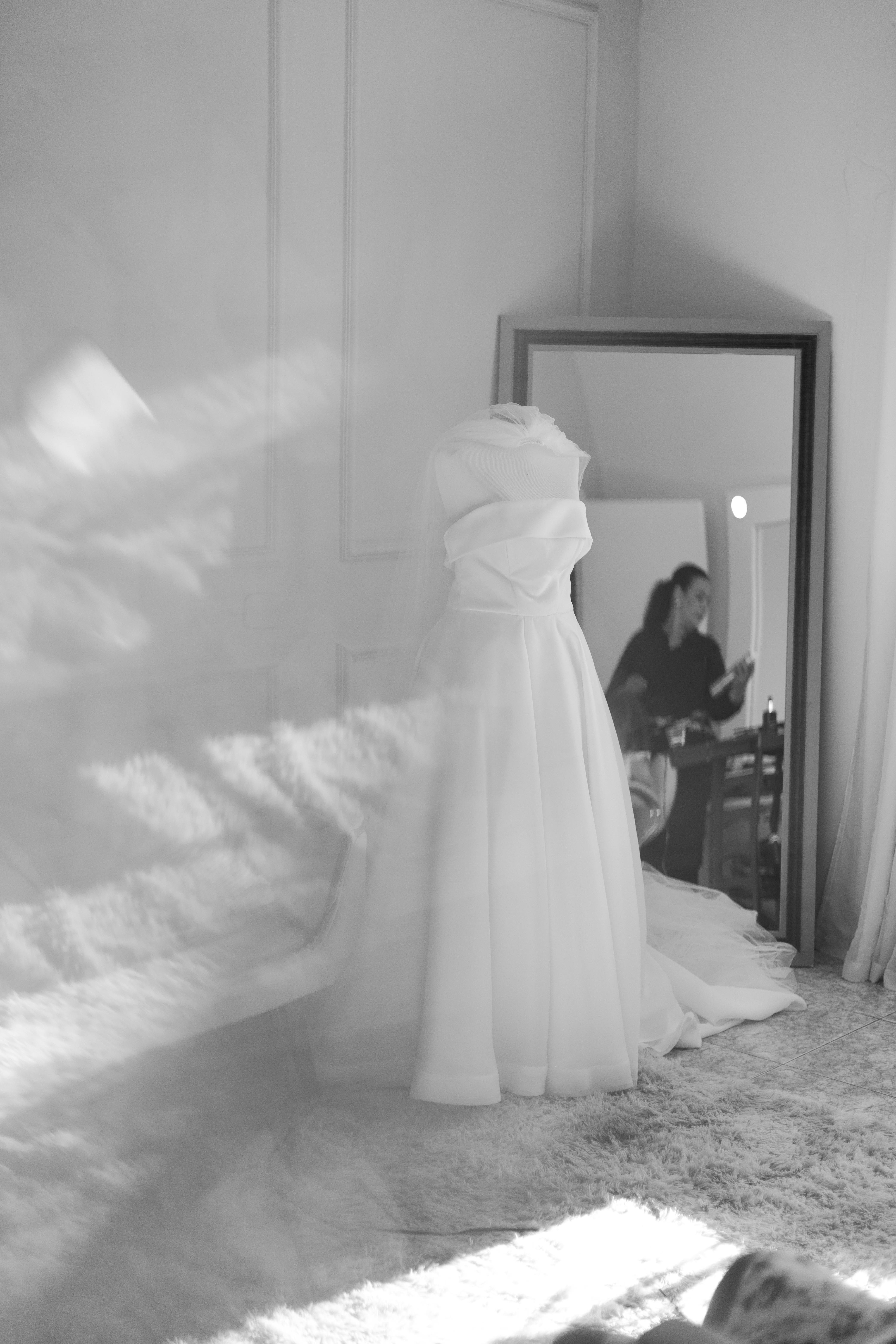Gratis Uno splendido abito da sposa bianco in una stanza luminosa con riflessi in uno specchio. Foto a disposizione
