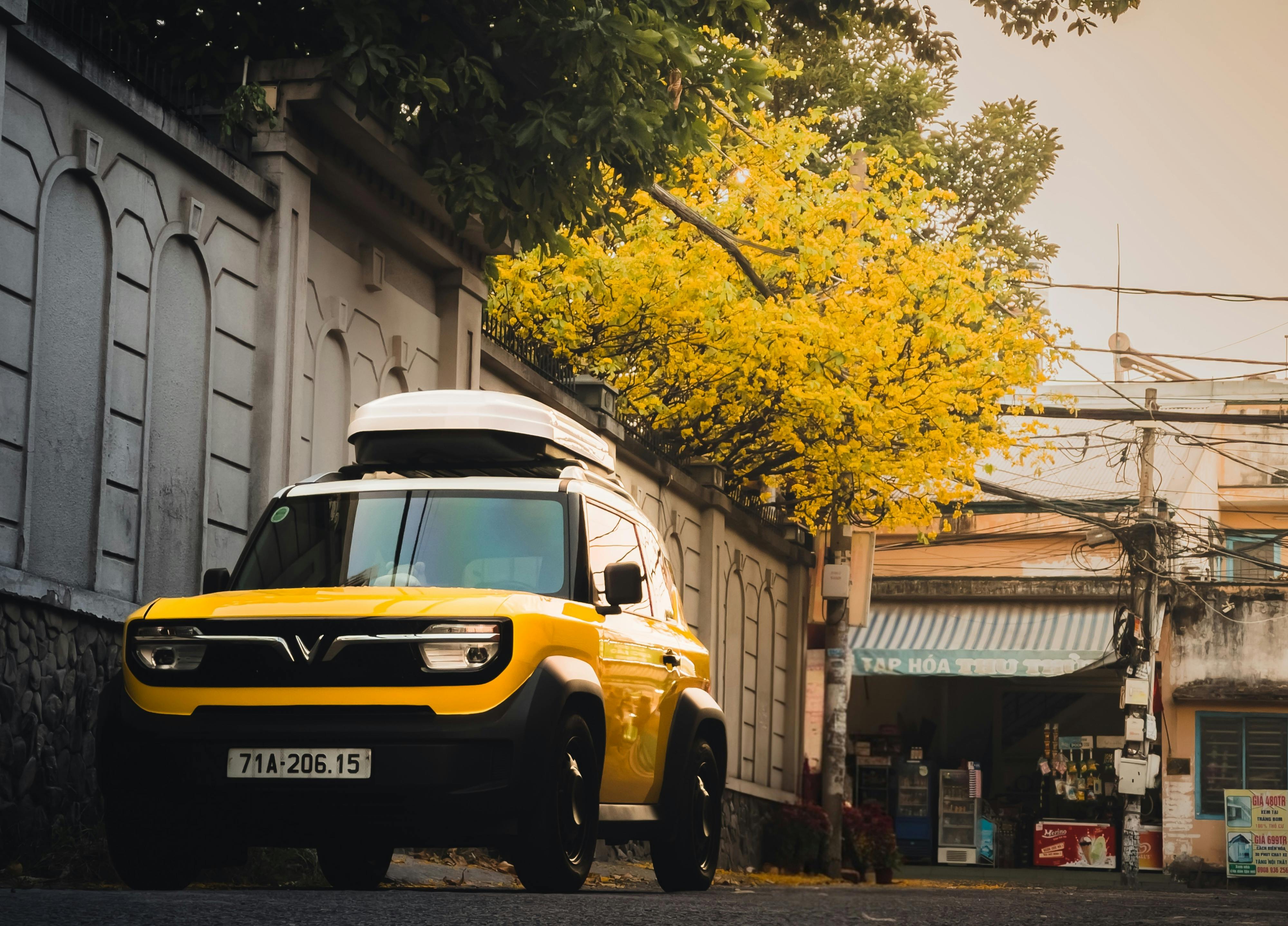 ฟรี รถเอสยูวีสีเหลืองสดใสจอดอยู่ริมถนนใต้ต้นไม้ที่กำลังออกดอก สะท้อนให้เห็นถึงแก่นแท้ของชีวิตในเมืองของเวียดนาม คลังภาพถ่าย