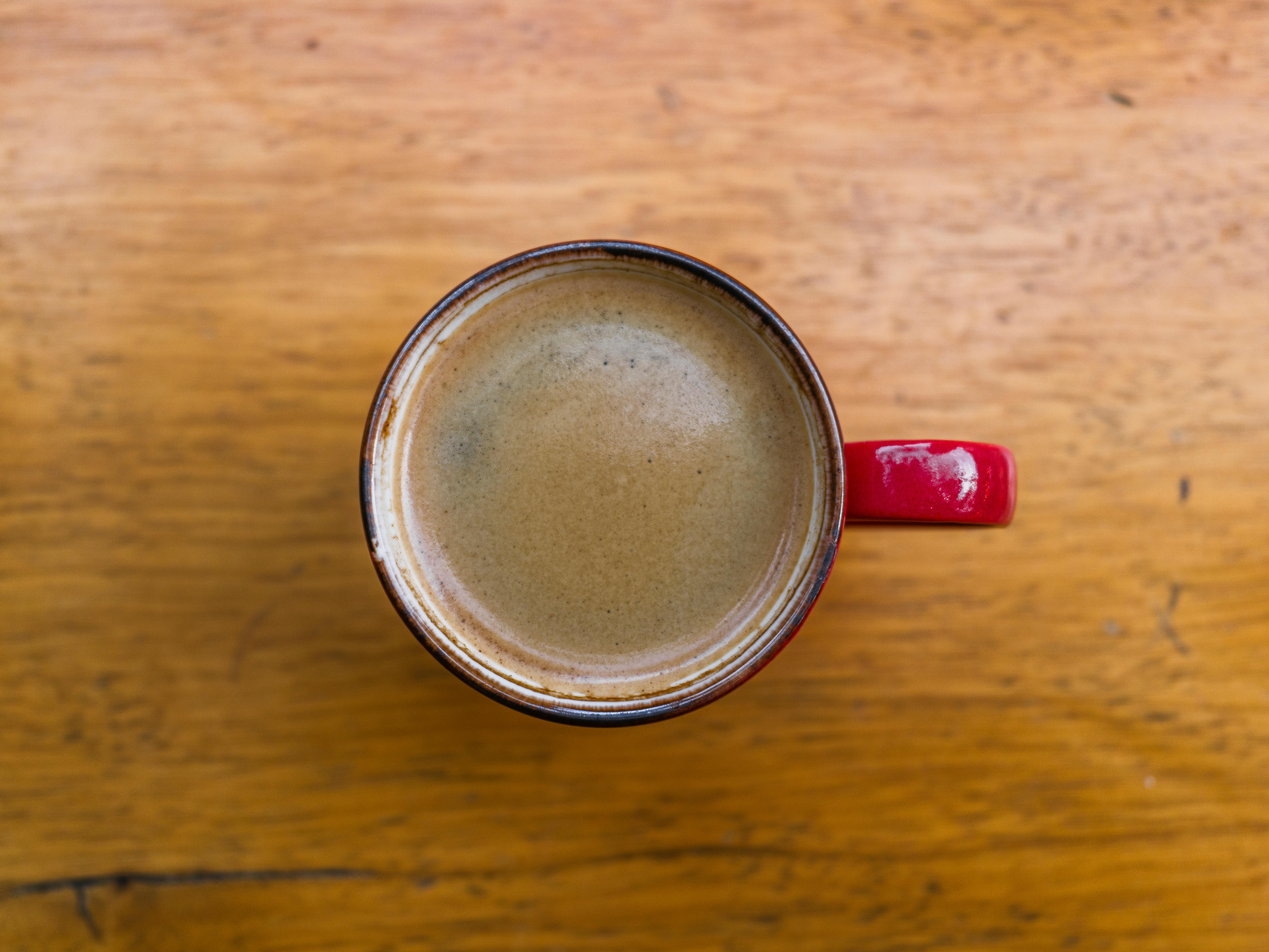 ฟรี ภาพระยะใกล้ของแก้วกาแฟสีแดงวางอยู่บนโต๊ะไม้สไตล์ชนบท ถ่ายจากมุมสูง คลังภาพถ่าย