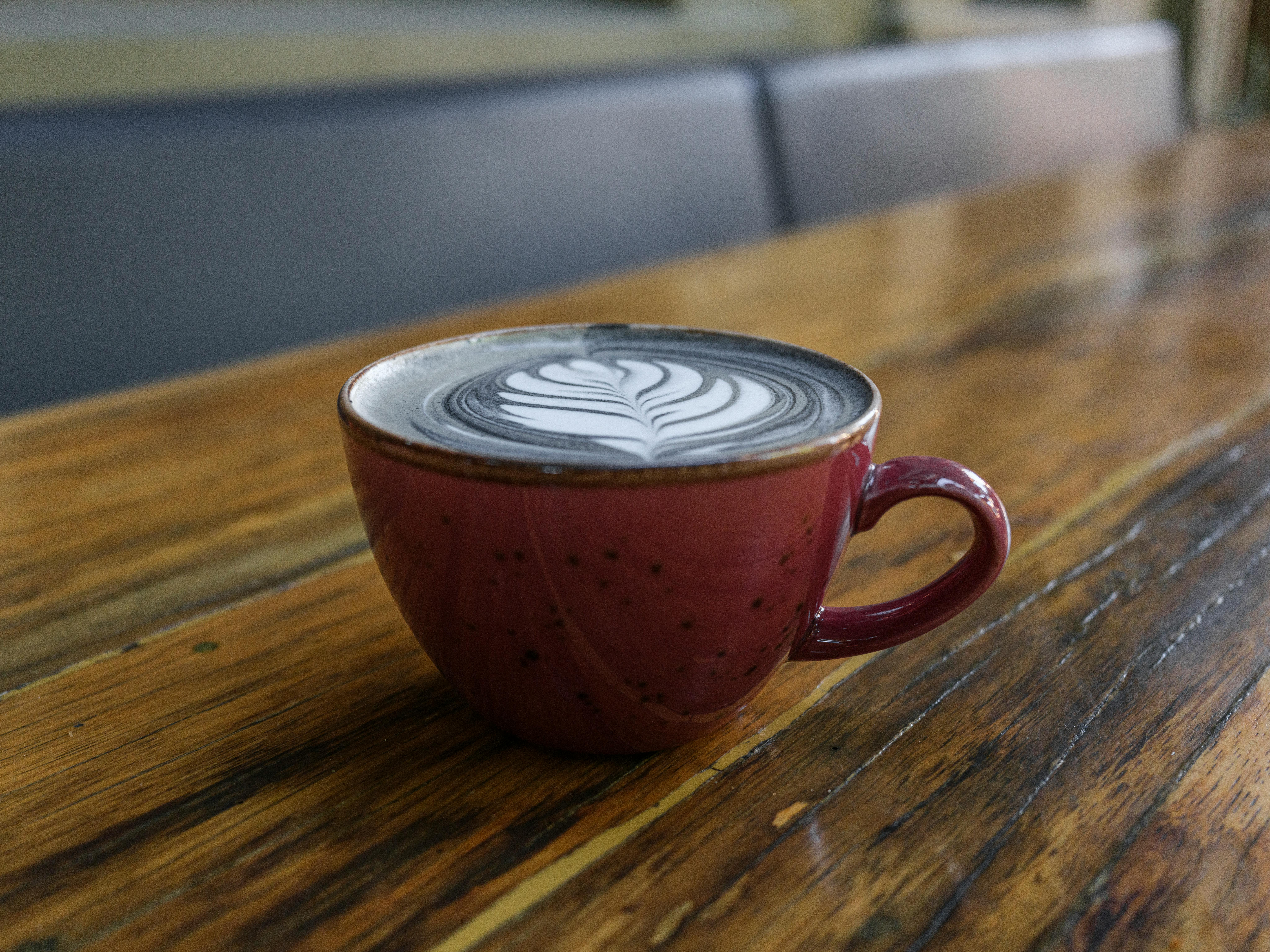 ฟรี ลาเต้ที่ตกแต่งอย่างสวยงามด้วยลวดลาย เสิร์ฟในแก้วเซรามิกสีแดงบนโต๊ะไม้ คลังภาพถ่าย