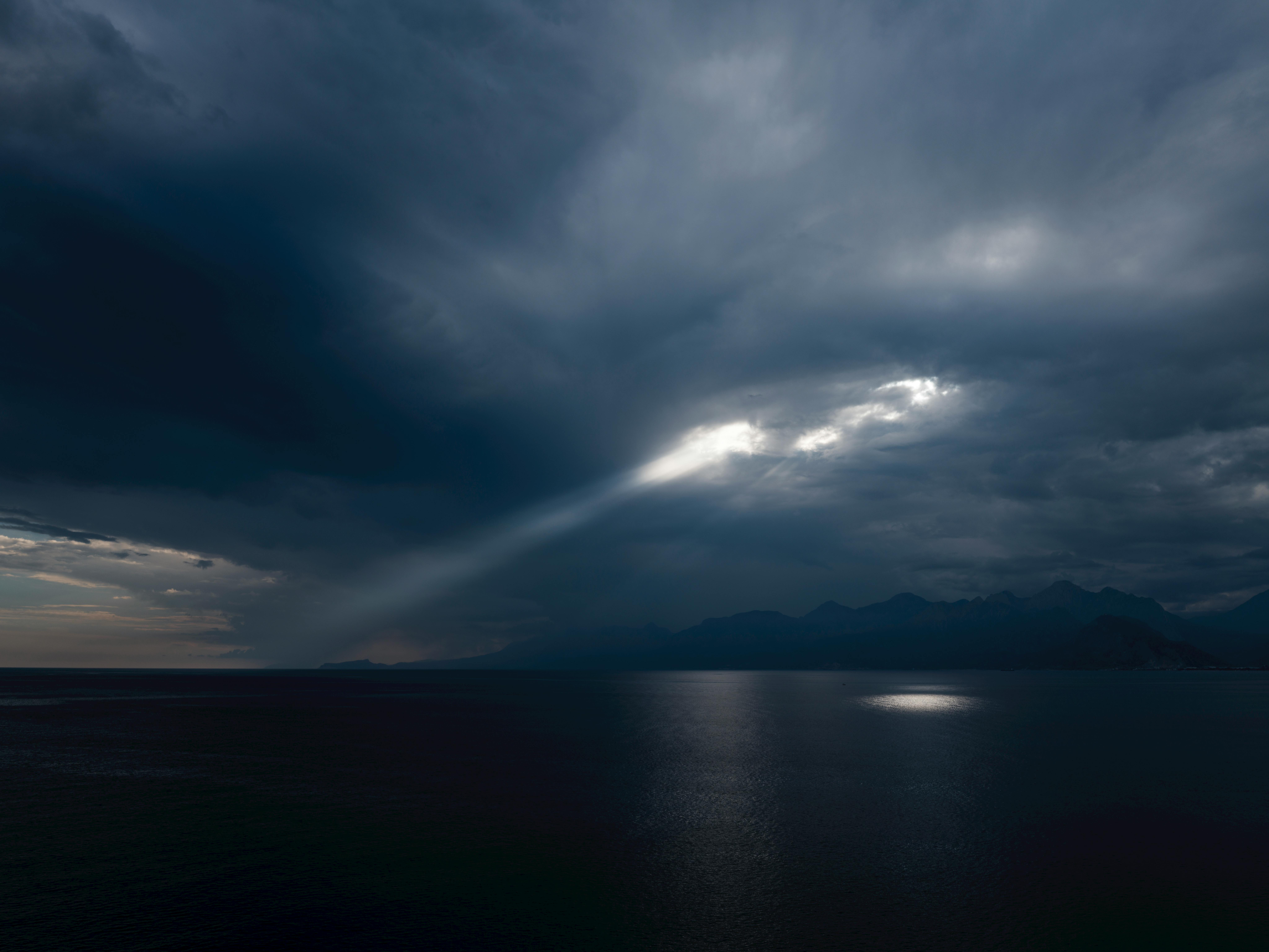 ฟรี ภาพทิวทัศน์ชายฝั่งอันงดงามที่แสงแดดส่องทะลุเมฆหนาทึบเหนือมหาสมุทร คลังภาพถ่าย