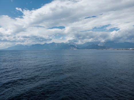Moody seascape with clouds over expansive ocean and distant coastal mountains.