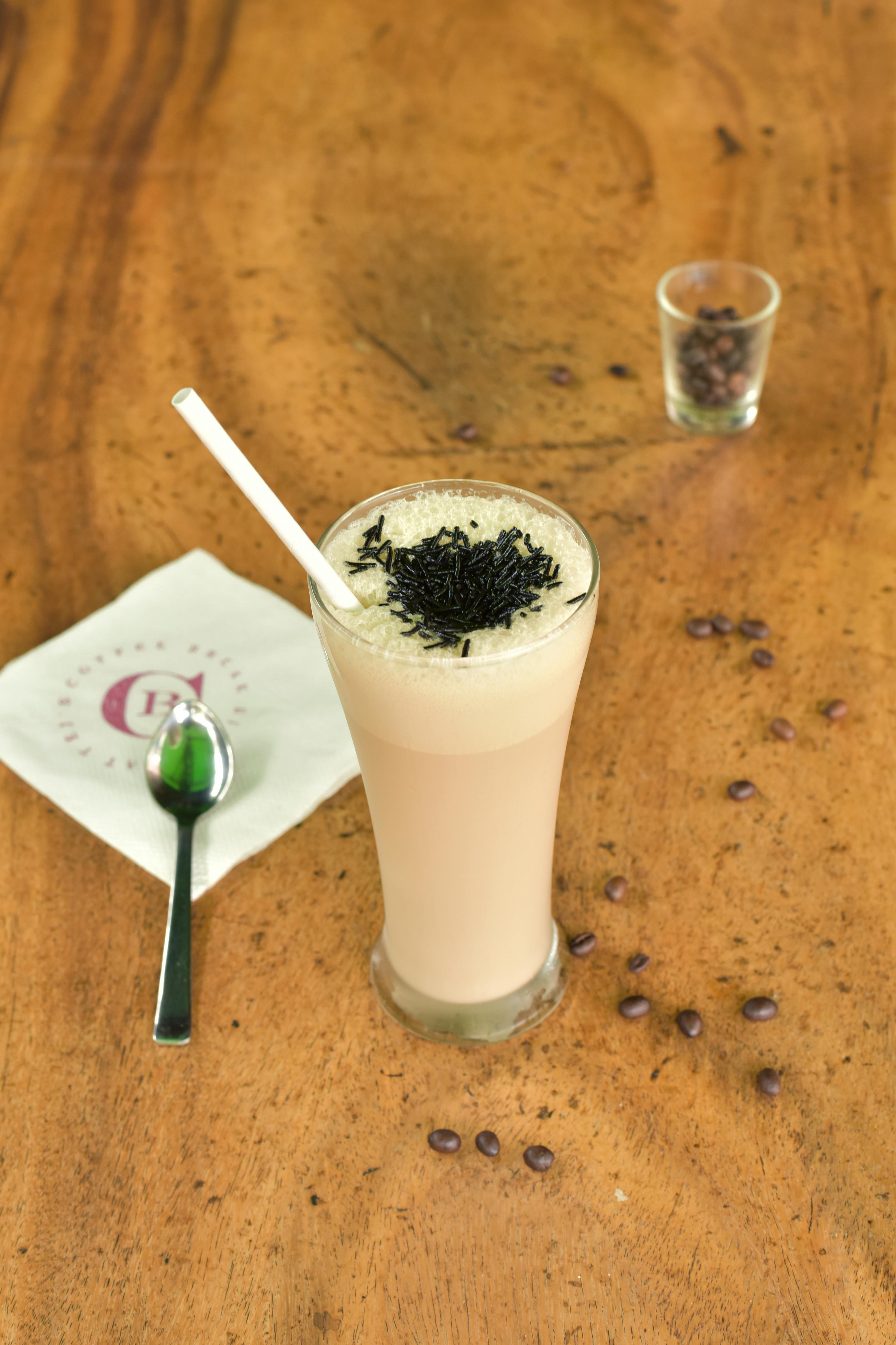 ฟรี กาแฟเย็นแก้วสูง โรยหน้าด้วยเกล็ดช็อกโกแลต วางอยู่บนโต๊ะไม้ คลังภาพถ่าย