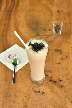 Tall glass of iced coffee topped with chocolate sprinkles on a wooden table.