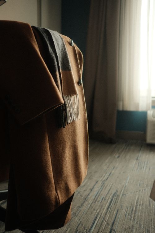 Free A fashionable camel coat with a wool scarf draped over a chair indoors, exuding warmth and style. Stock Photo