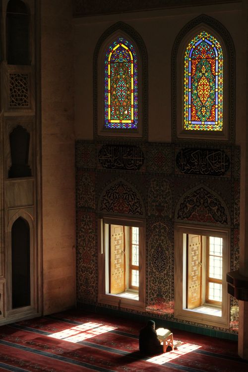 Free Sunlit mosque interior with intricate stained glass and a person in prayer, creating a serene ambiance. Stock Photo
