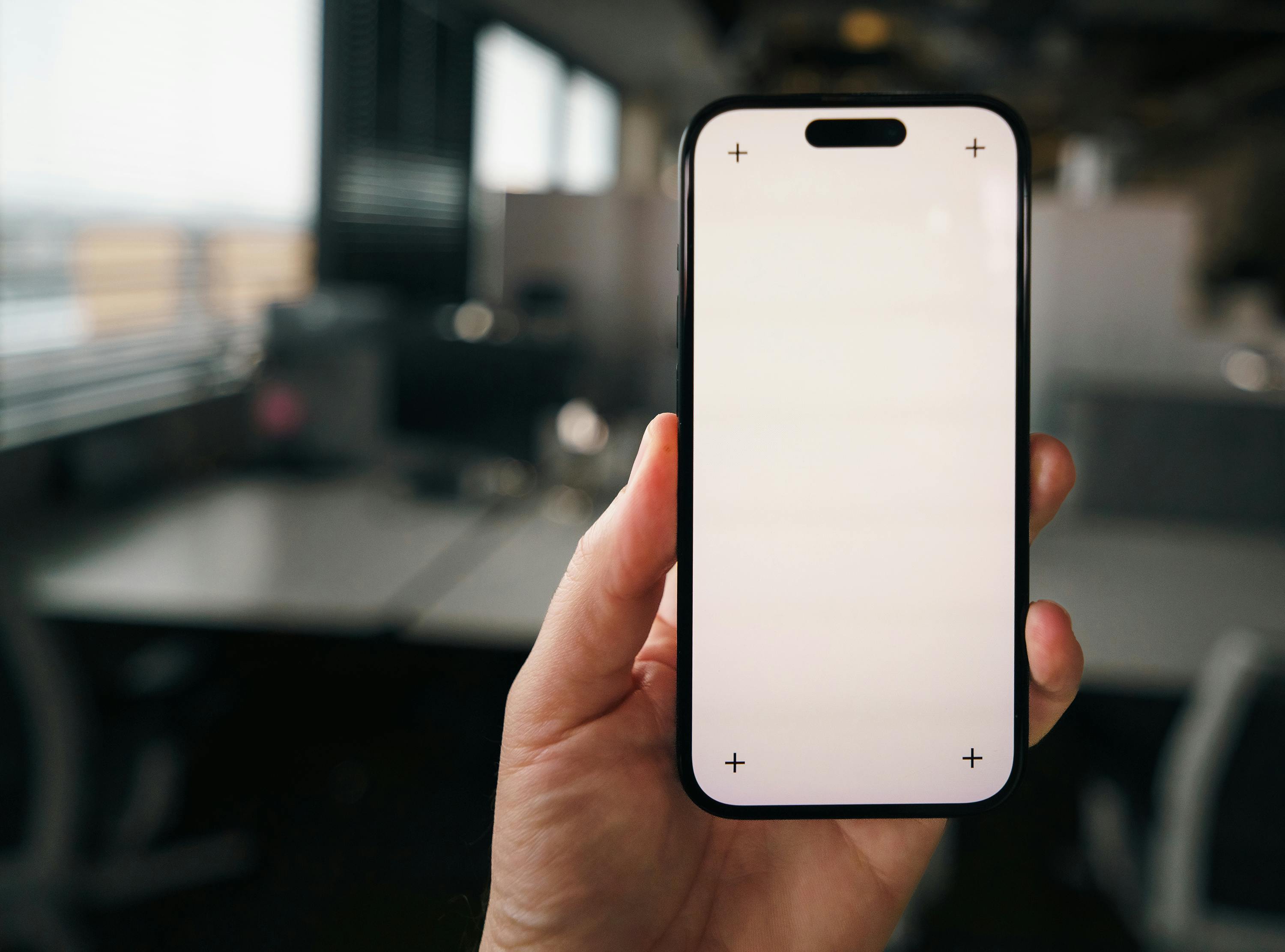 bezplatná Ruka držící maketu prázdné obrazovky smartphonu v moderním kancelářském prostředí, ideální pro prezentaci aplikací. Základová fotografie