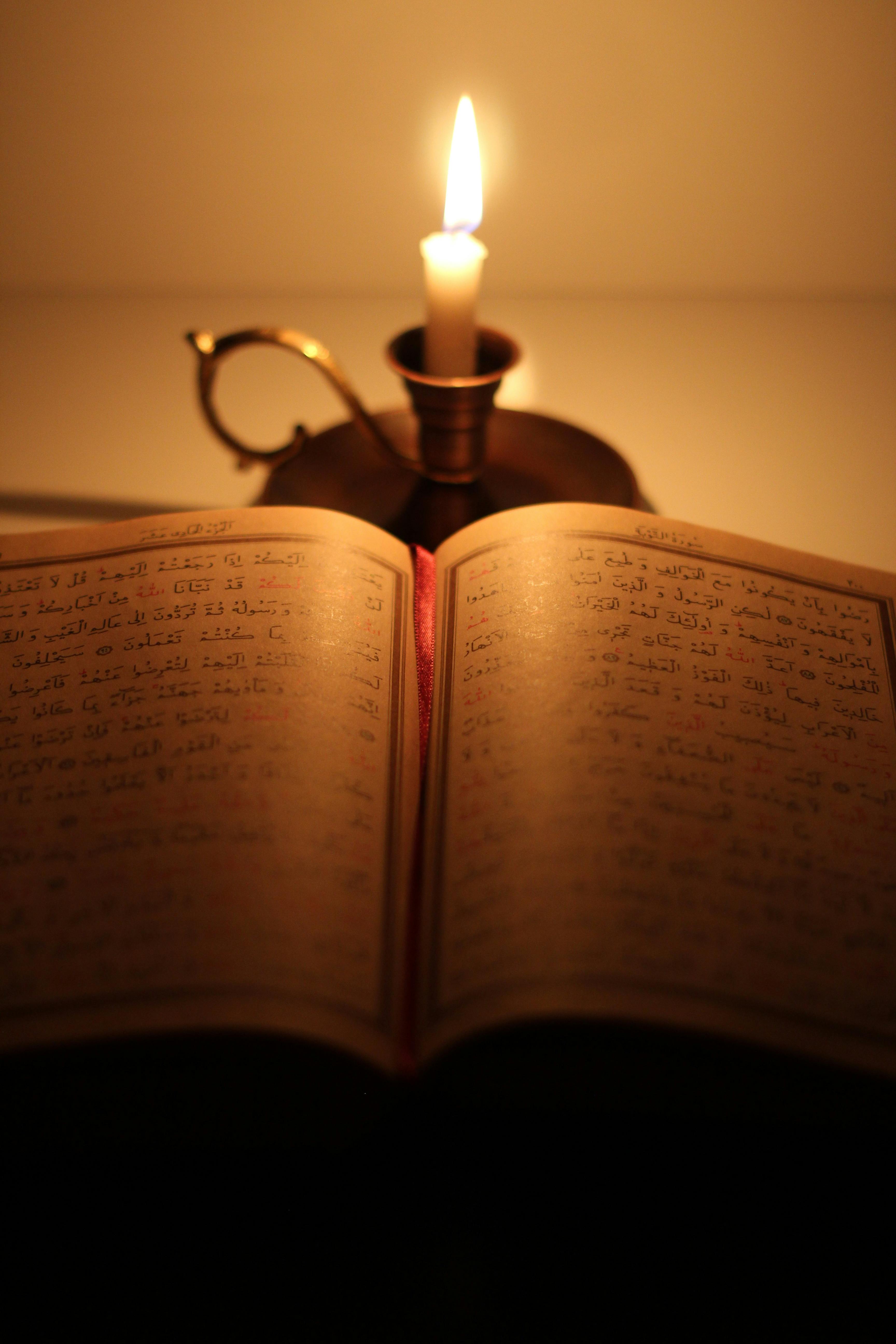 A Quran open next to a glowing candle, creating a serene and warm religious setting.