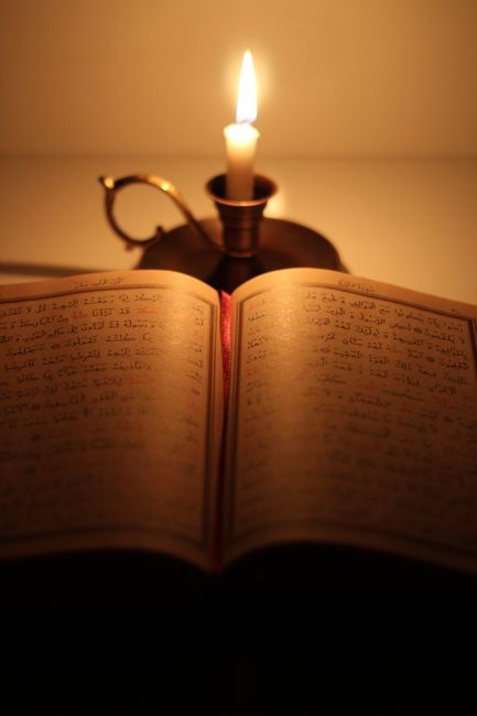 2026'da Sahur Nedir? Sahurla İlgili Hadisler ve Güncel Uygulamalar 5 A Quran open next to a glowing candle, creating a serene and warm religious setting.