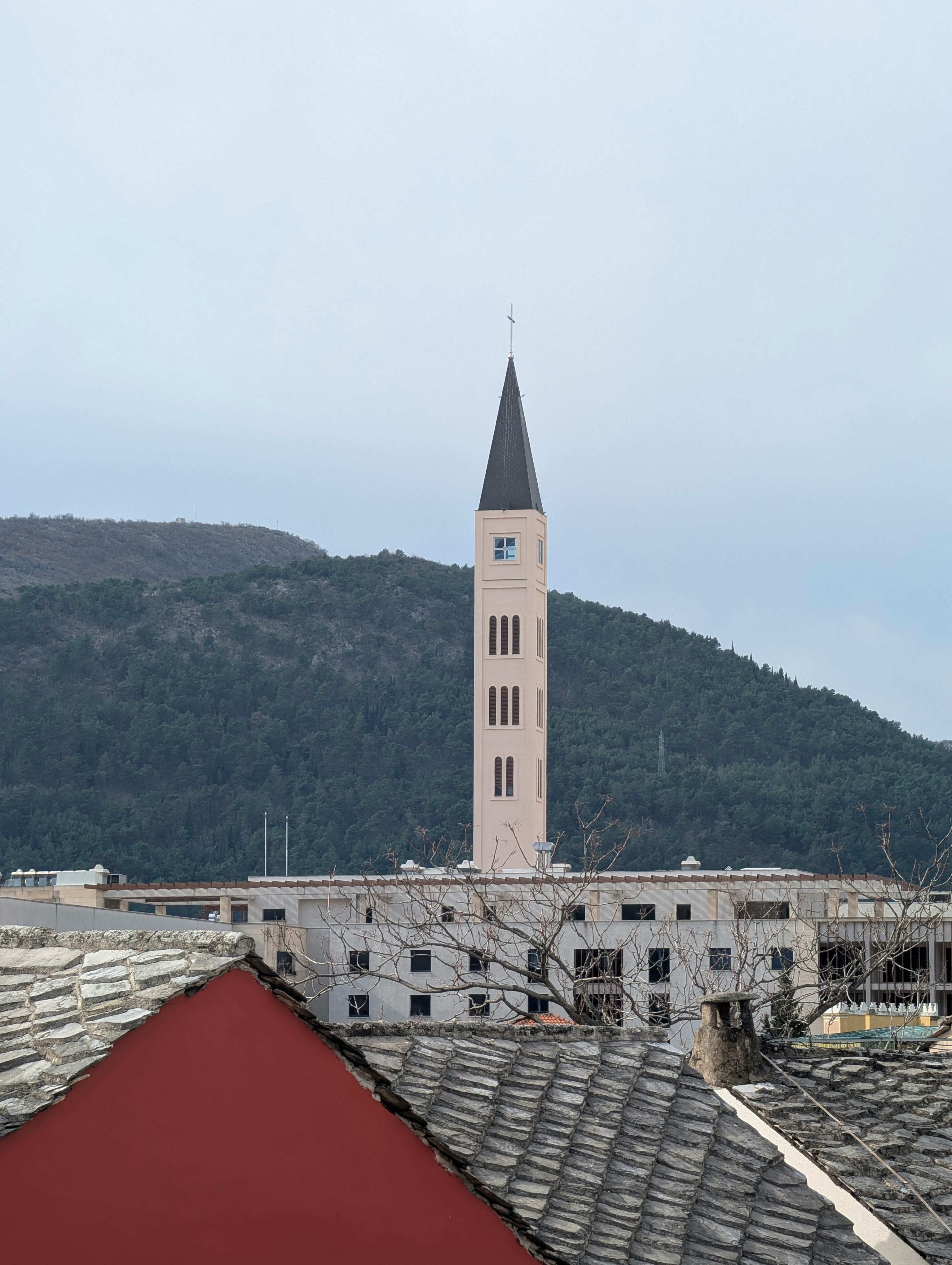 bezplatná Vysoká kostelní věž s ostrou špicí zasazená do horského pozadí za zamračeného dne. Základová fotografie
