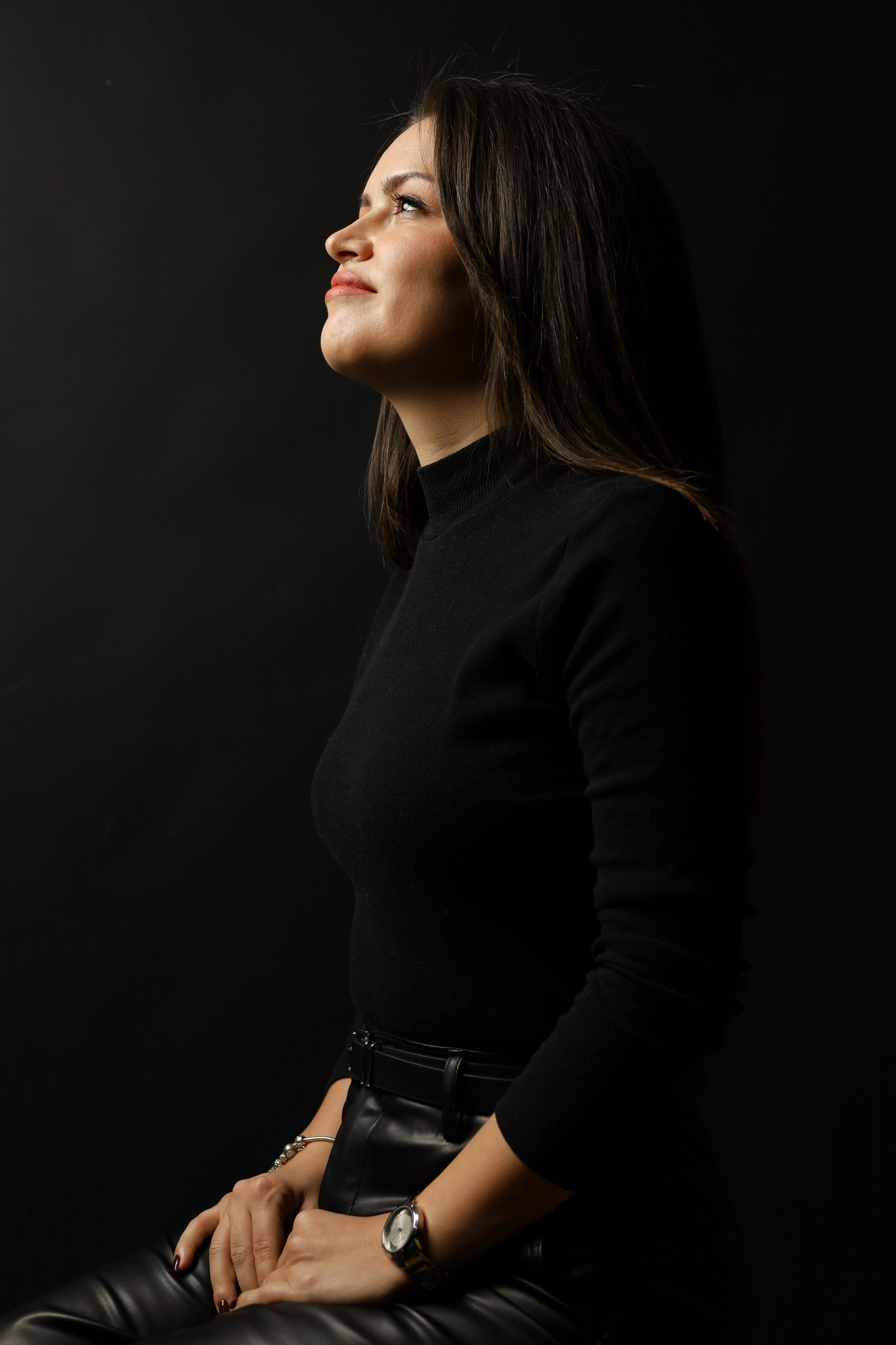 Profile portrait of a woman in black attire against a dark studio background, exuding elegance.