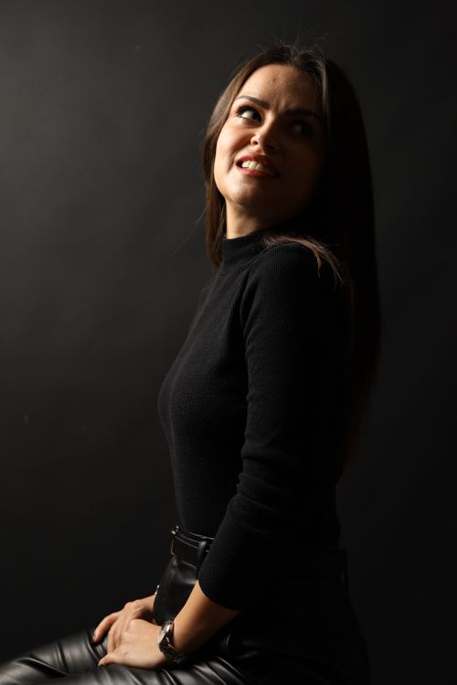 Free Stylish woman in black sweater seated against dark backdrop, exuding elegance. Stock Photo