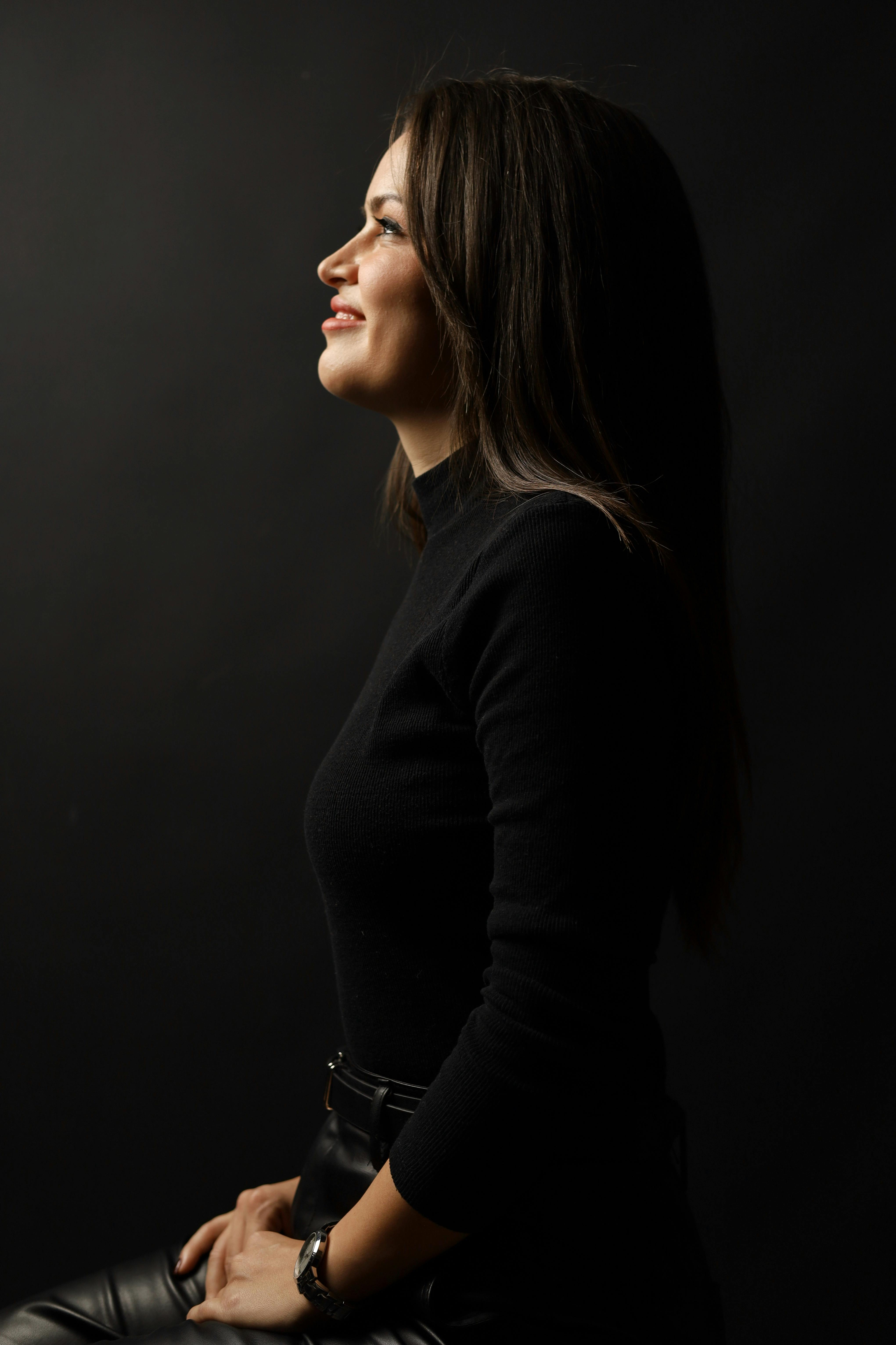 Side profile portrait of a smiling woman in a black outfit against a dark background, exuding warmth and confidence.