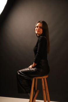 Elegant woman sitting on a stool in a professional studio. Artistic portrait.