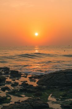Beautiful sunrise over the ocean with rocky shoreline and calm waves.