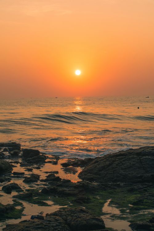 Free Beautiful sunrise over the ocean with rocky shoreline and calm waves. Stock Photo