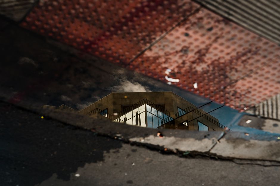 Reflection of a modern architectural building in a sidewalk puddle with textured surfaces.