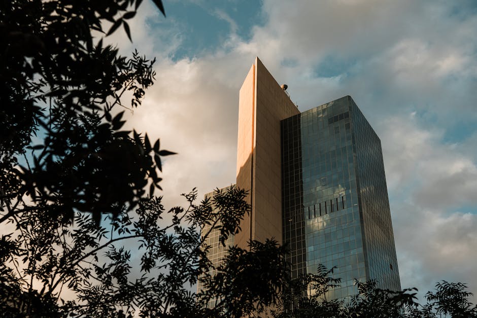 A modern skyscraper surrounded by trees against a dramatic sunset sky in Phoenix, Arizona.