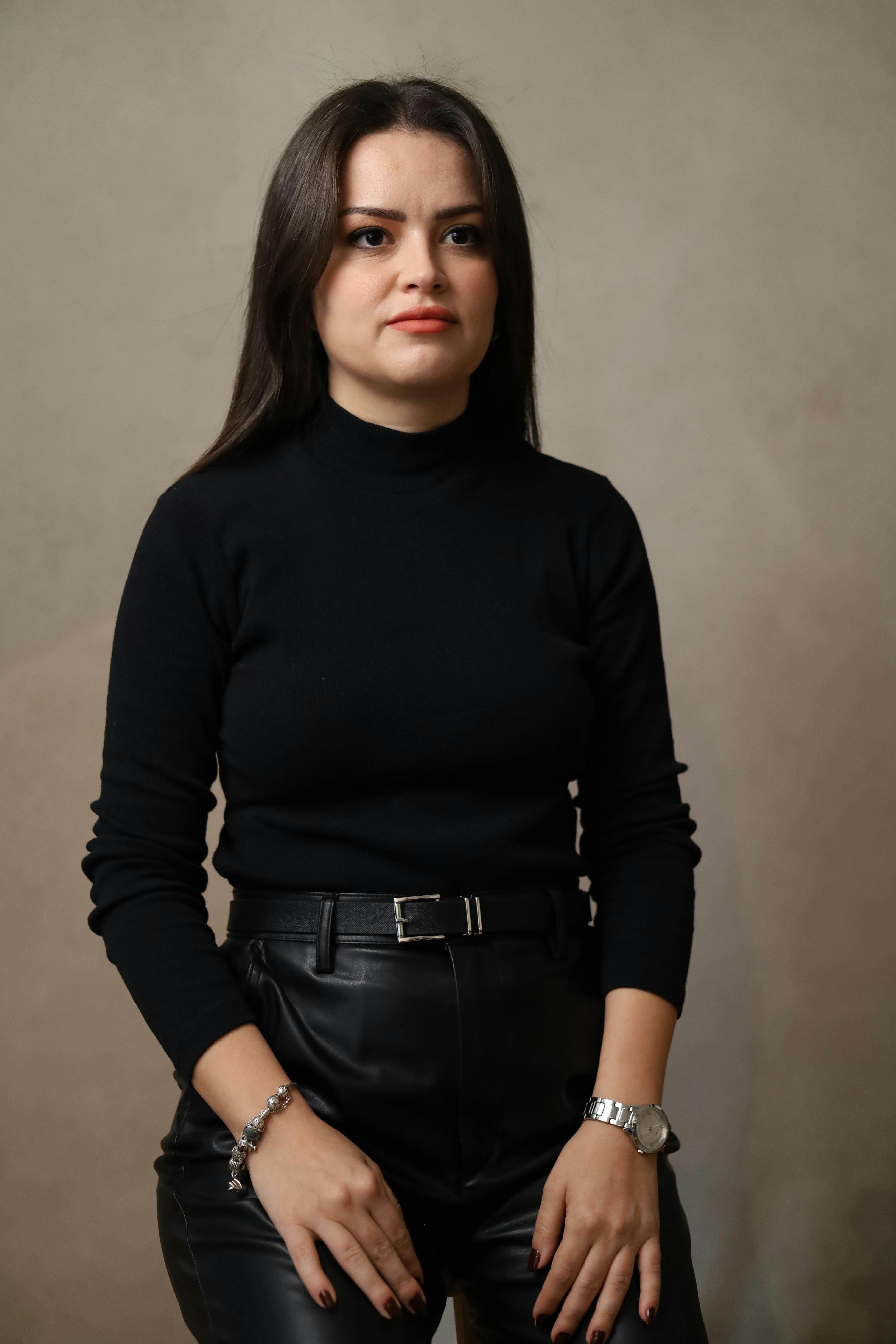 Gratis Elegante ritratto di una donna in pantaloni e top di pelle nera su uno sfondo neutro, che trasmette sicurezza. Foto a disposizione