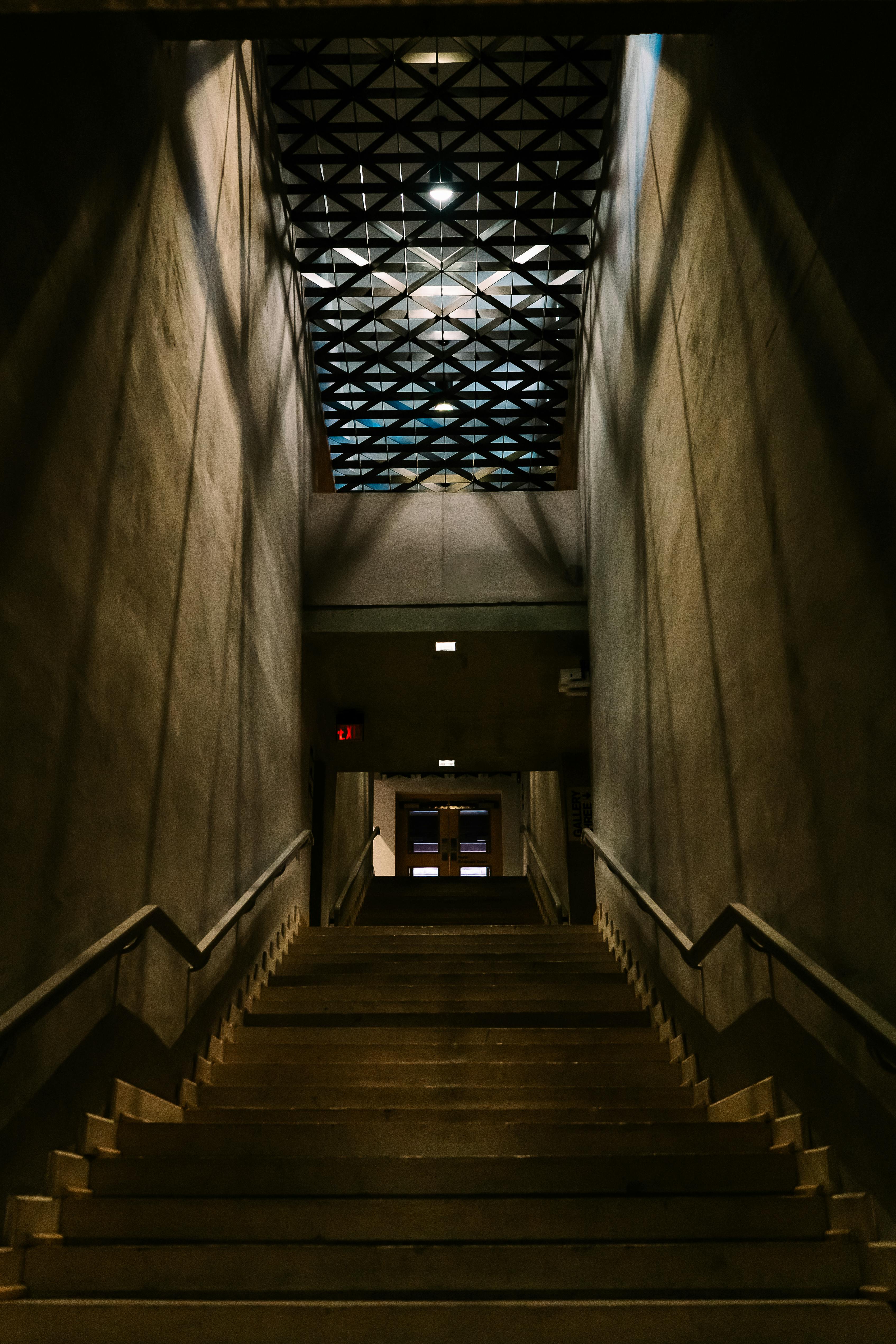 Gratis En svakt opplyst trapp med geometriske takmønstre som skaper en dramatisk atmosfære innendørs. Arkivbilde