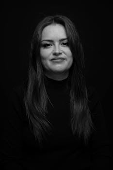 Elegant black and white portrait of a woman wearing a black turtleneck against a dark background.