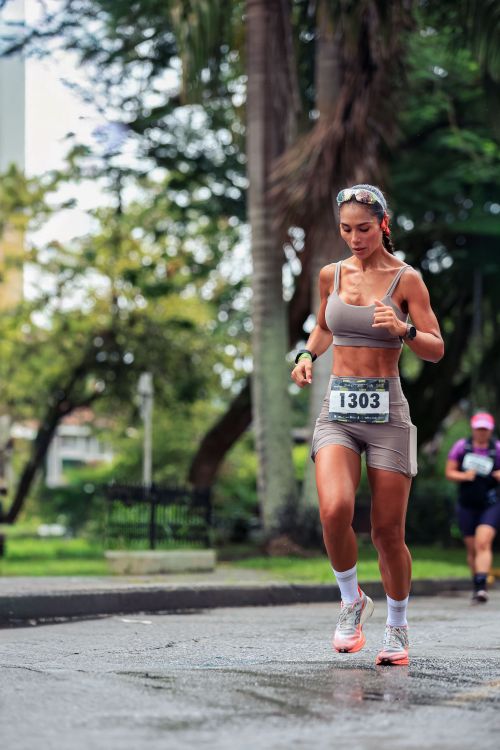 Free Focused female runner competing in a marathon on a rainy street, showing determination and athleticism. Stock Photo