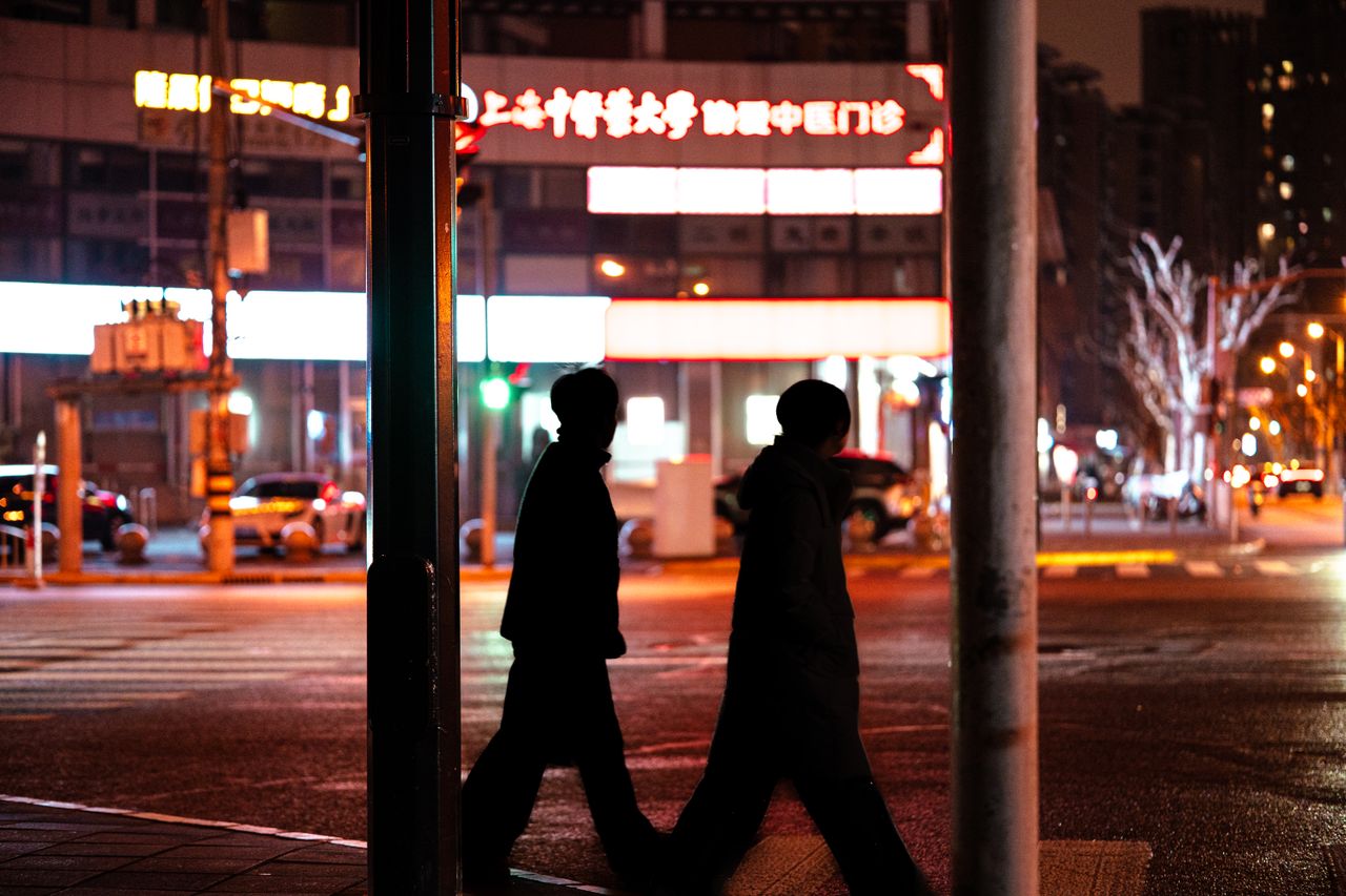 silhouetted figures crossing a city street at night under vibrant city