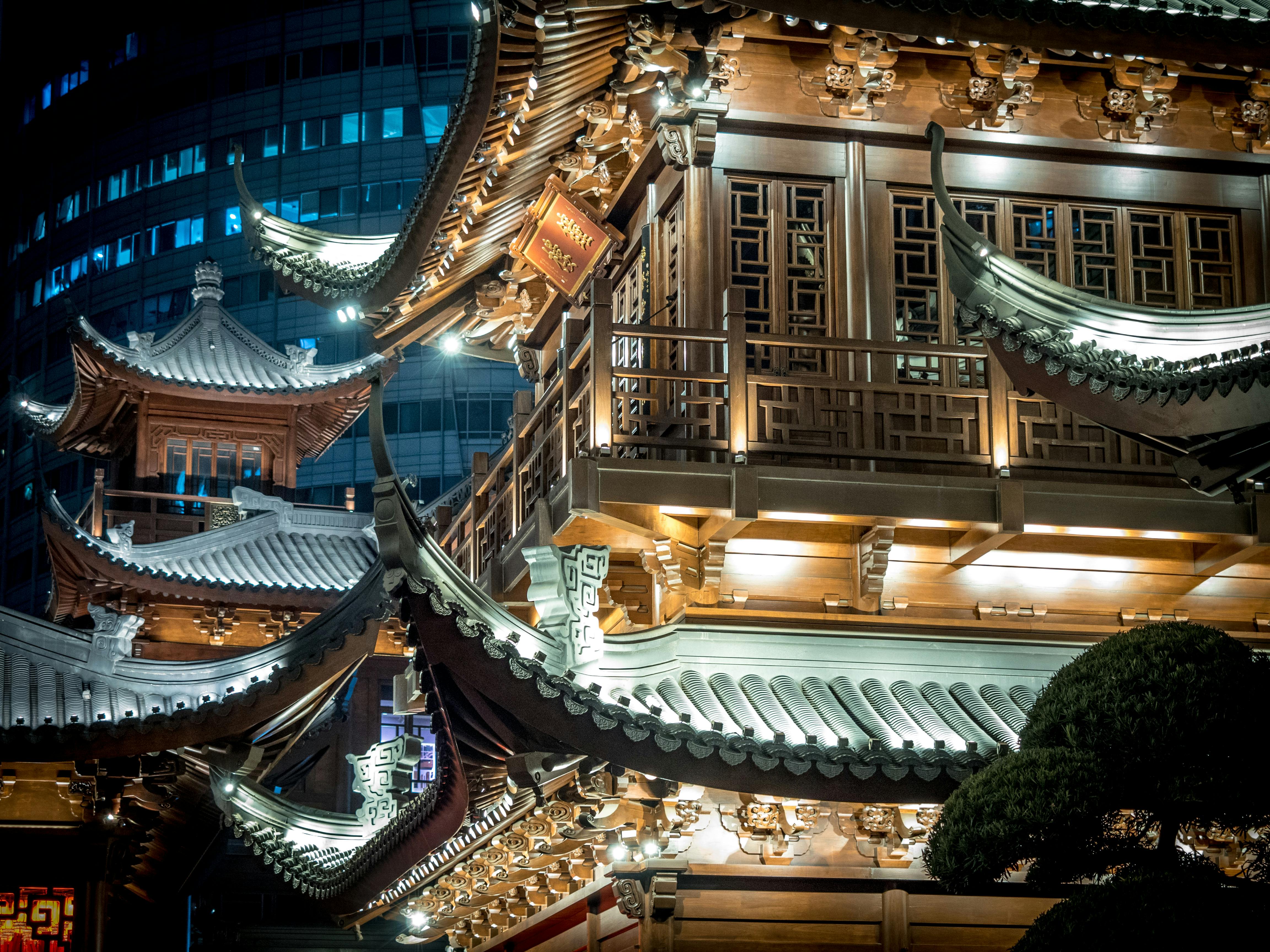 ฟรี สถาปัตยกรรมเอเชียที่ซับซ้อนส่องสว่างในยามค่ำคืน เผยให้เห็นงานแกะสลักไม้ที่ประณีต คลังภาพถ่าย