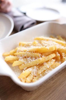 Golden French fries topped with freshly grated Parmesan cheese in a ceramic dish.