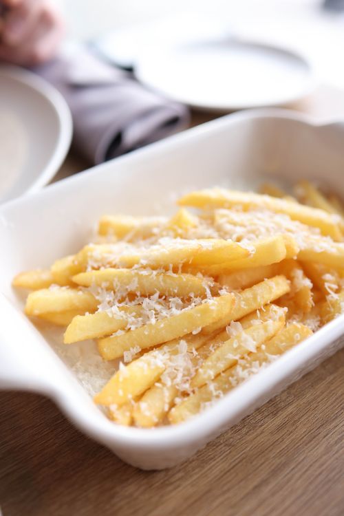 Free Golden French fries topped with freshly grated Parmesan cheese in a ceramic dish. Stock Photo