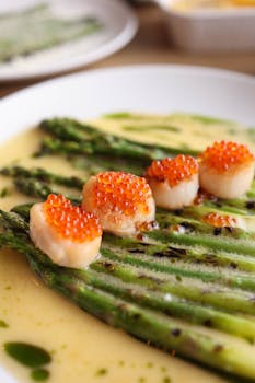 A close-up of grilled asparagus topped with scallops and roe on a creamy sauce.