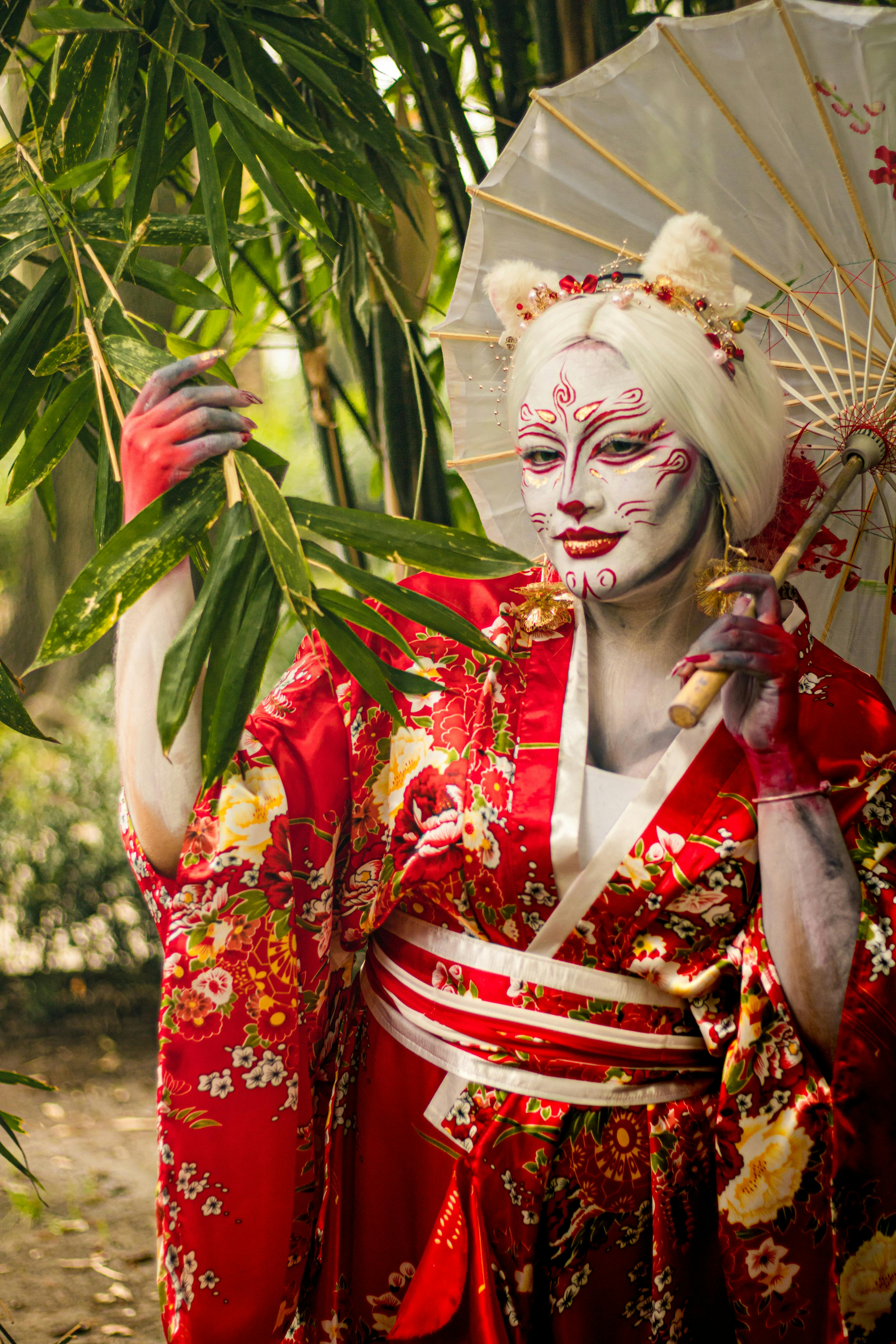 Ücretsiz Bambu korusunda şemsiye altında poz veren, sanatsal makyajlı kırmızı kimono giymiş bir geyşa. Stok Fotoğraflar